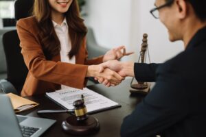 Woman lawyer hand and women client shaking hand collaborate on working agreements with contract documents at the modern office.