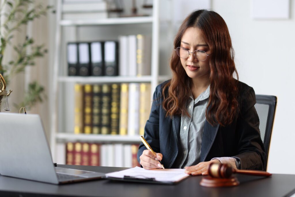 Woman sitting at desk signing document on the table next to a laptop and gavel