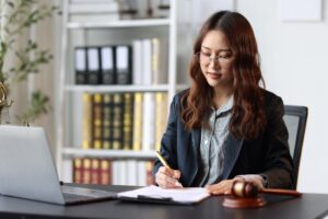 Woman sitting at desk signing document on the table next to a laptop and gavel