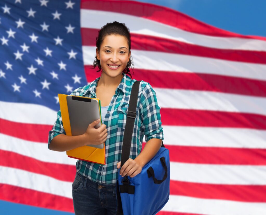 Smiling female holding a bookbag and books in front of an american flag