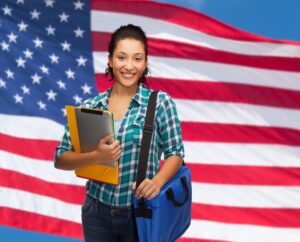 Smiling female holding a bookbag and books in front of an american flag
