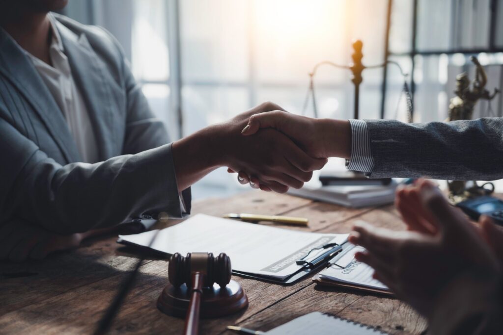 two people shaking hands with a clipboard and gavel on desk