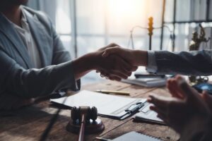two people shaking hands with a clipboard and gavel on desk