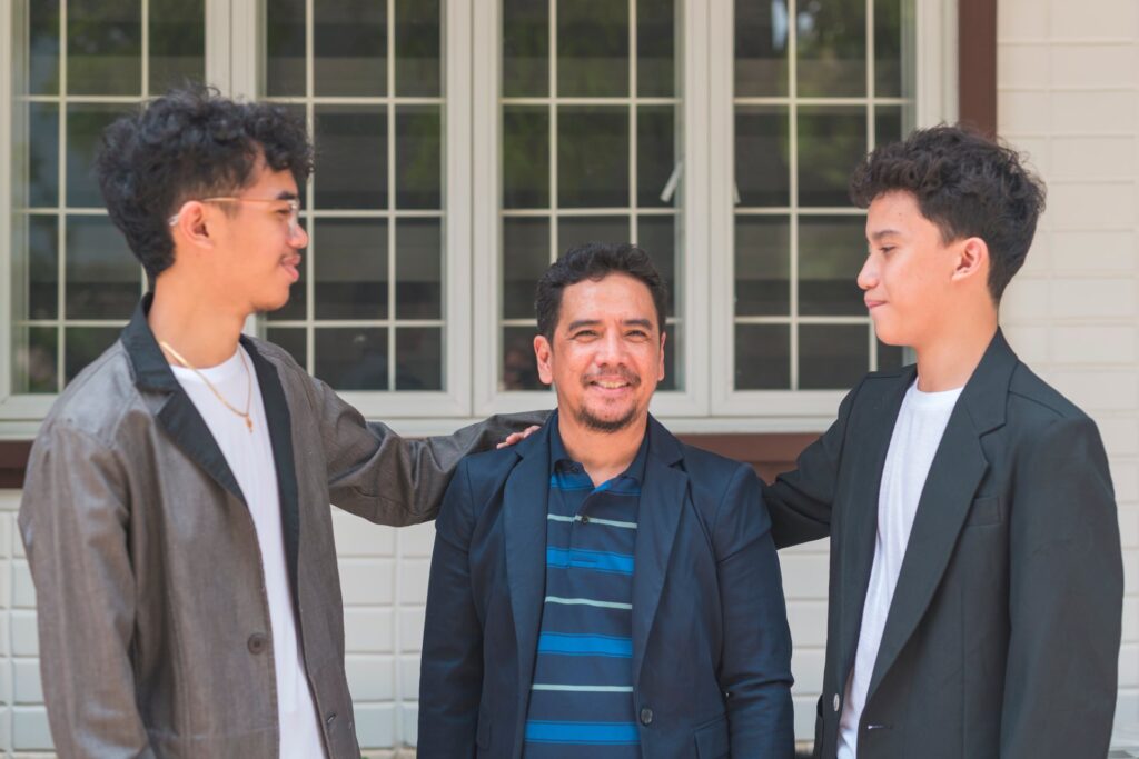 One shorter man surrounded by two younger kids with their hands on his shoulders