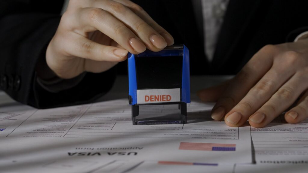 A close up of a person holding a stamp that says denied on a USA visa