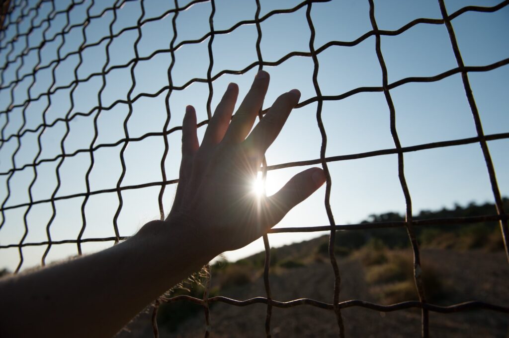 A human hand touching a gate with the sun reflecting on it