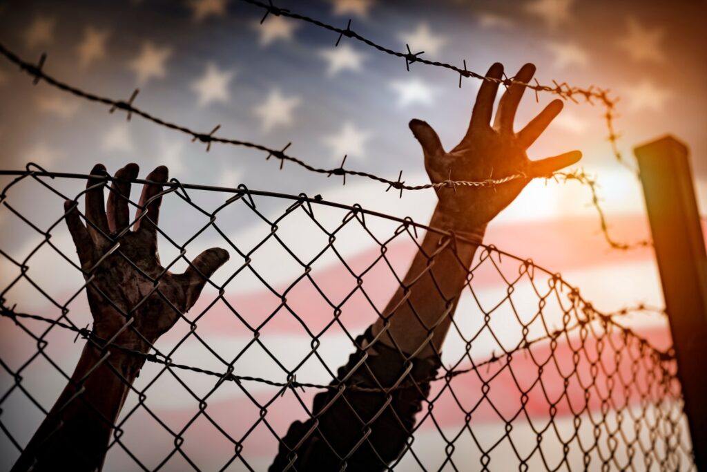Hands climbing over a fence with a united states flag in the background