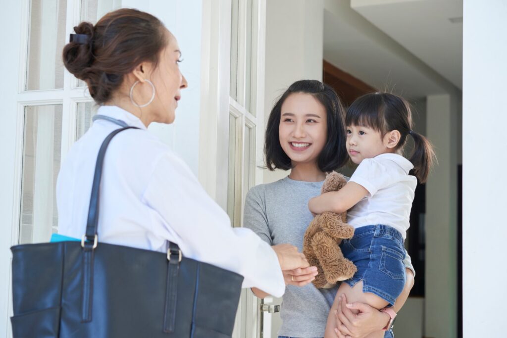 Woman standing in her doorway holding a child talking to another woman outside of her house