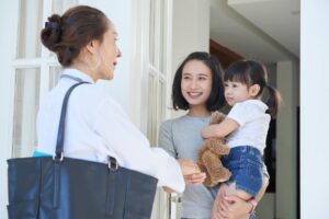 Woman standing in her doorway holding a child talking to another woman outside of her house