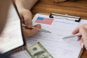 A hand holding a pen pointing to a visa application paperwork on a clipboard with money on top
