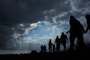 Multiple Immigrants walking outside with a blue sky and dark clouds.