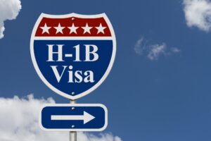 Blue and red road sign displaying H-1B visa with an arrow, set against a blue sky and clouds