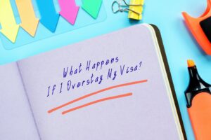 A notebook that says "what happens if I overstay my visa? on a blue background next to an orange highlighter