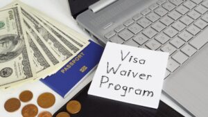 A sticky note that says visa waiver program next to a laptop, money and a passport
